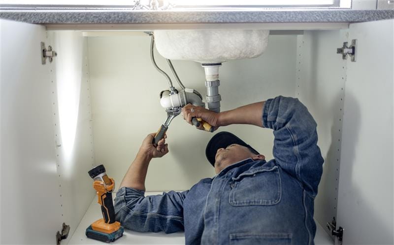 Plumber repairing pipes beneath a bathroom sink in Port Orange
