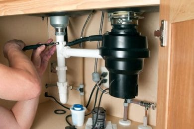 Plumber repairing a garbage disposal beneath a kitchen sink in Port Orange