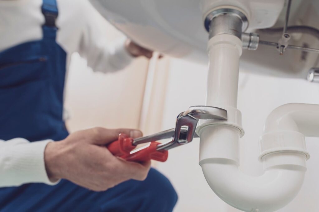 Plumber repairing a white drain pipe beneath a sink in Port Orange